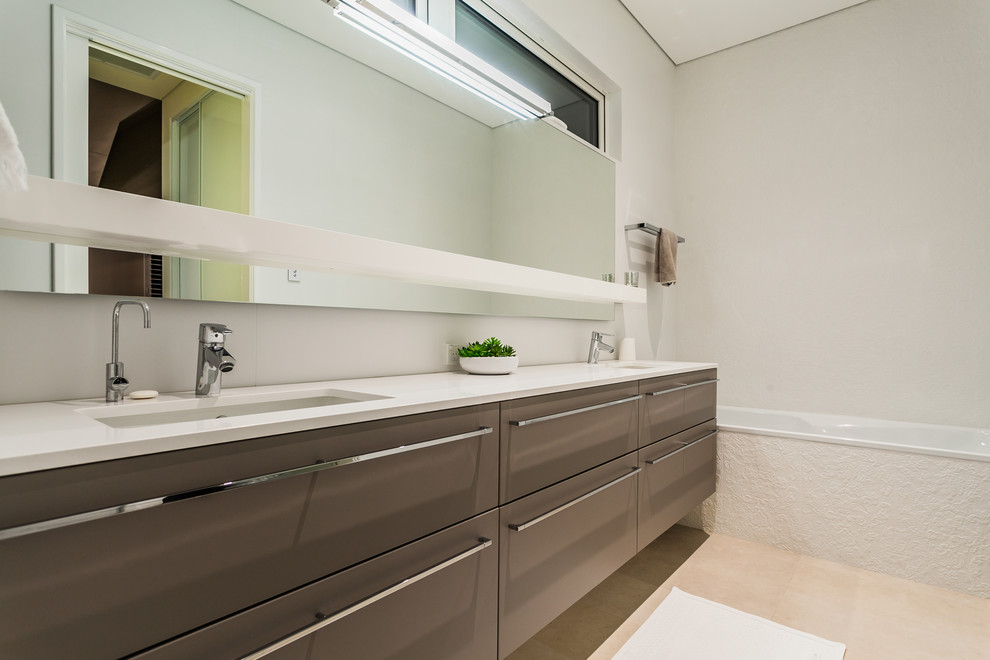 Réalisation d'une salle de bain design avec un placard à porte plane, des portes de placard marrons, une baignoire en alcôve, un mur blanc et un lavabo encastré.