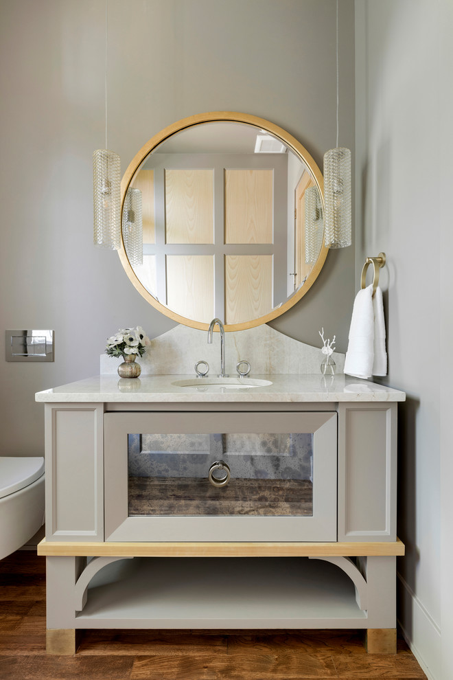 Bild på ett lantligt beige beige badrum, med grå skåp, en vägghängd toalettstol, grå väggar, mellanmörkt trägolv, ett undermonterad handfat, brunt golv och luckor med infälld panel