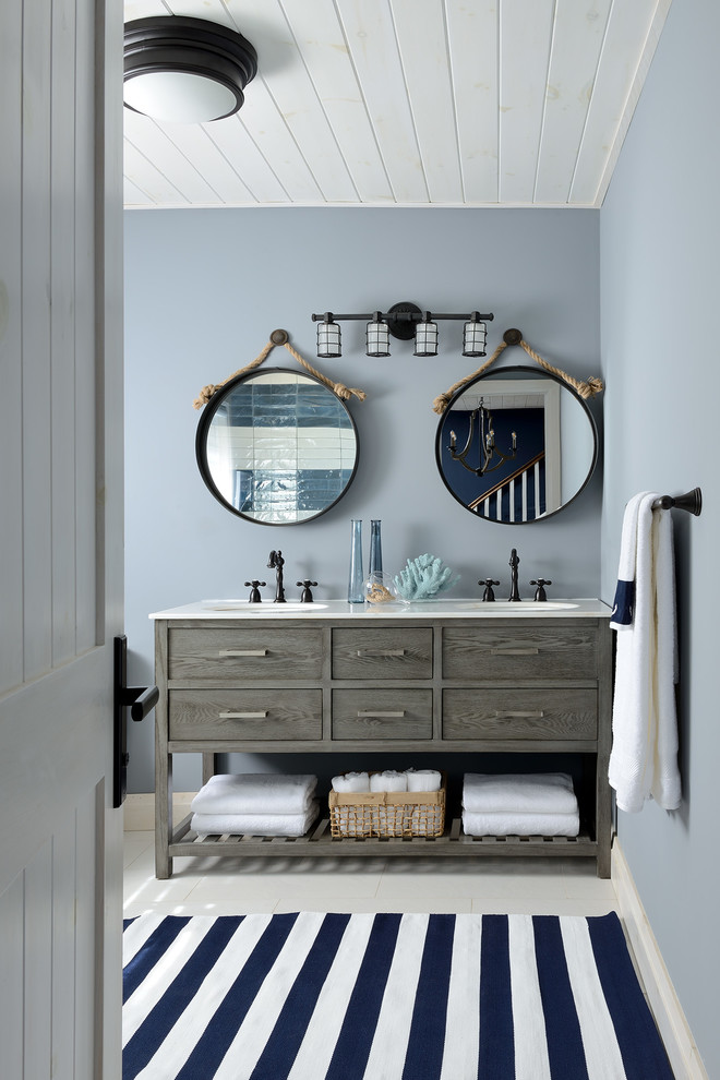 Cette photo montre une salle de bain bord de mer avec un placard à porte plane, des portes de placard grises, un mur bleu et un sol blanc.
