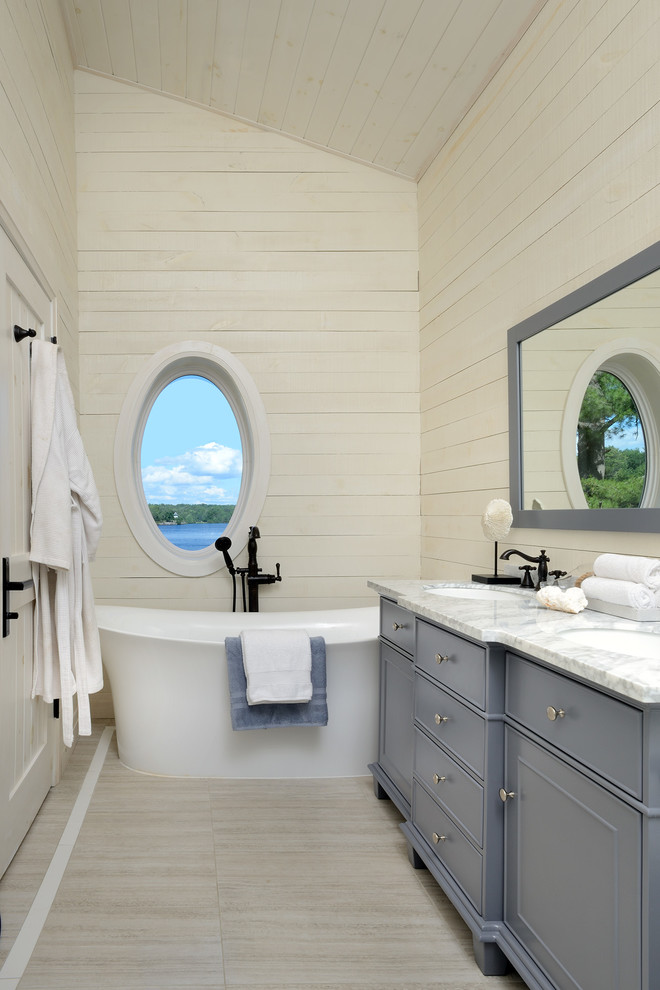Cette image montre une salle de bain marine avec un placard à porte plane, des portes de placard grises, une baignoire indépendante, un mur blanc, parquet clair, un lavabo encastré et un sol blanc.