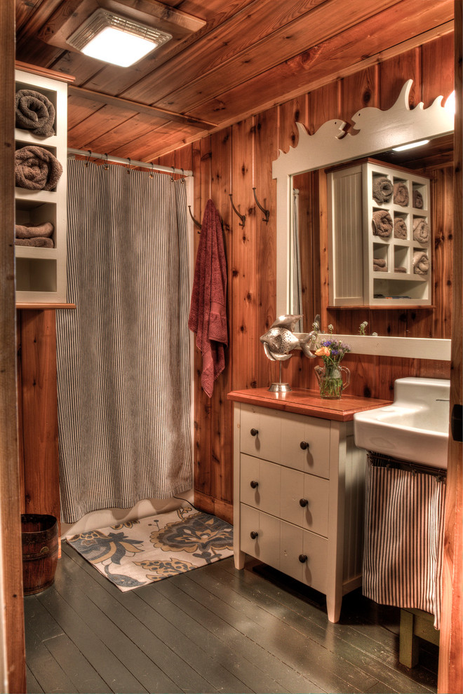 Diseño de cuarto de baño rústico con suelo de madera pintada, lavabo tipo consola, puertas de armario beige, encimera de madera, bañera empotrada y combinación de ducha y bañera