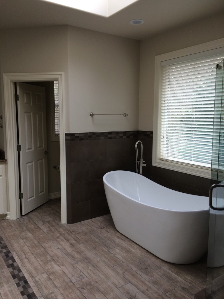 Cette image montre une salle de bain principale design de taille moyenne avec un placard avec porte à panneau surélevé, des portes de placard blanches, une baignoire indépendante, une douche d'angle, un carrelage gris, des carreaux de porcelaine, un mur blanc, un sol en bois brun, un plan de toilette en granite, un sol gris et une cabine de douche à porte battante.