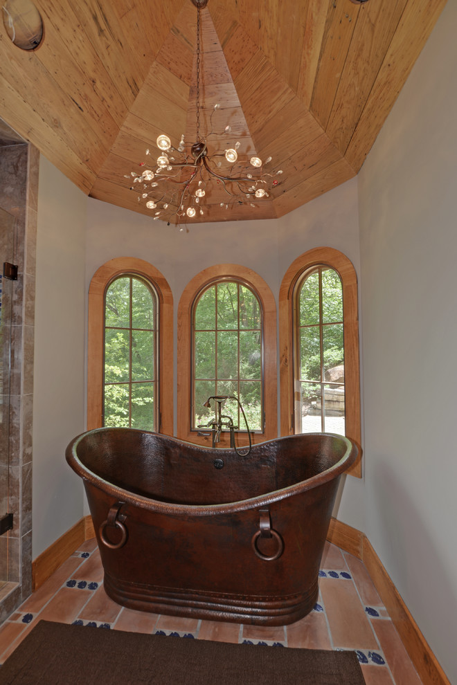 Idée de décoration pour une salle de bain chalet avec une baignoire indépendante et tomettes au sol.
