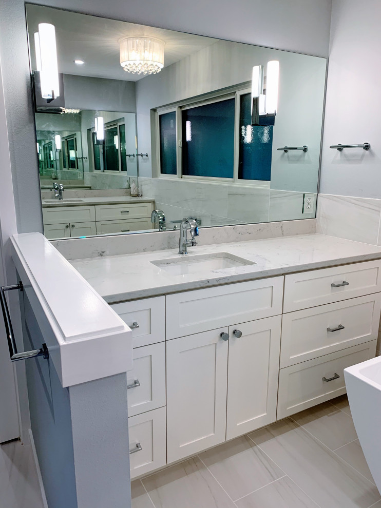 Пример оригинального дизайна: большая главная ванная комната в стиле неоклассика (современная классика) с фасадами в стиле шейкер, белыми фасадами, отдельно стоящей ванной, открытым душем, серой плиткой, мраморной плиткой, серыми стенами, мраморным полом, врезной раковиной, столешницей из искусственного кварца, серым полом, душем с распашными дверями, серой столешницей, тумбой под одну раковину, встроенной тумбой, фартуком и нишей