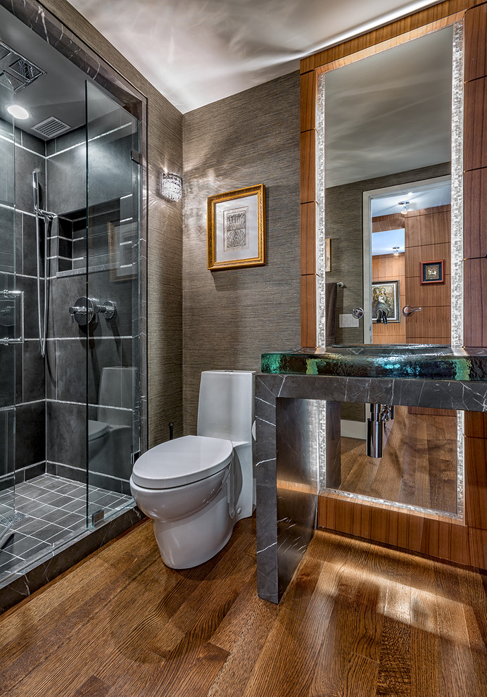 This is an example of a traditional bathroom in Chicago with open cabinets, grey cabinets, a corner shower, a one-piece toilet, black tiles, grey walls, medium hardwood flooring, a console sink, brown floors and a hinged door.