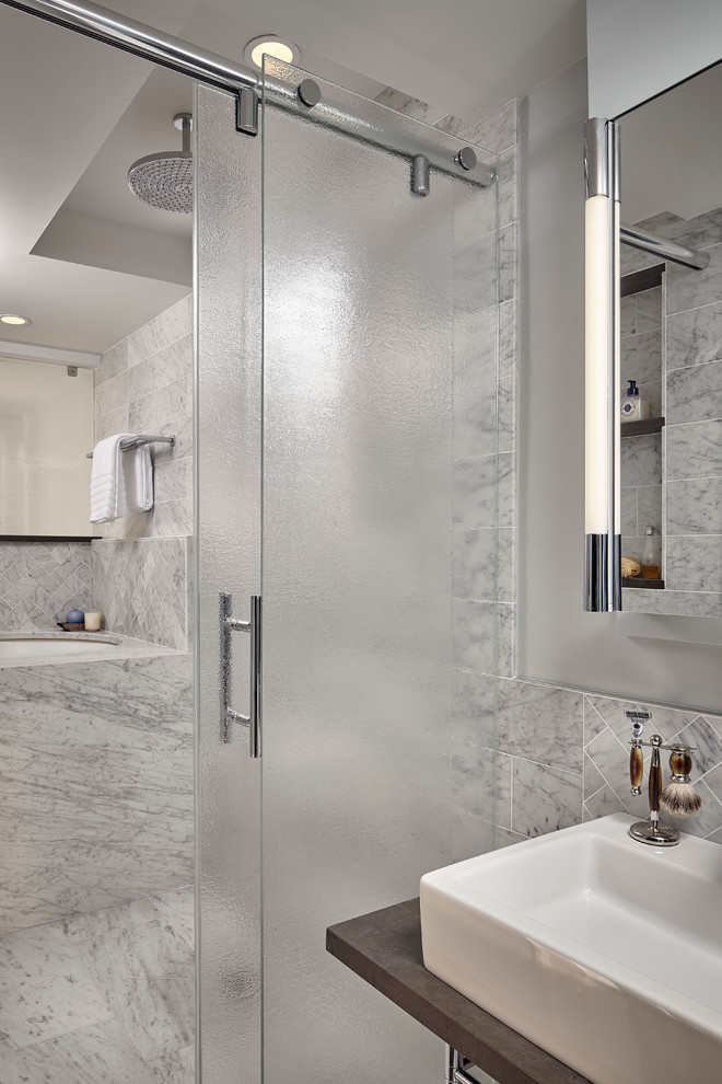 Cette photo montre une salle de bain tendance avec un combiné douche/baignoire, un carrelage gris, un carrelage de pierre, un mur gris, un sol en marbre, un plan vasque, un plan de toilette en calcaire, une cabine de douche à porte coulissante et une baignoire encastrée.