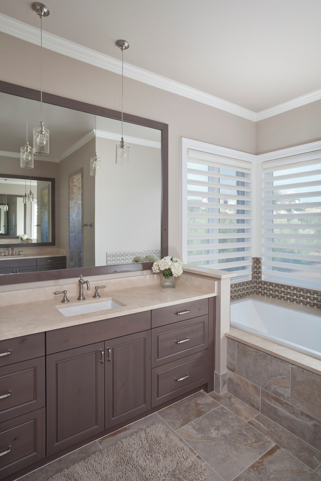 Immagine di una stanza da bagno tradizionale con lavabo sottopiano, ante con bugna sagomata, vasca da incasso, pareti beige e ante in legno bruno