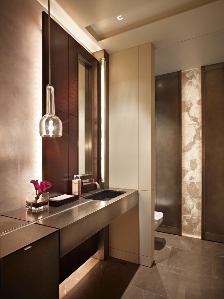 Imagen de cuarto de baño principal contemporáneo de tamaño medio con lavabo bajoencimera, encimera de acero inoxidable, baldosas y/o azulejos de piedra, sanitario de una pieza, paredes beige, suelo marrón y encimeras grises