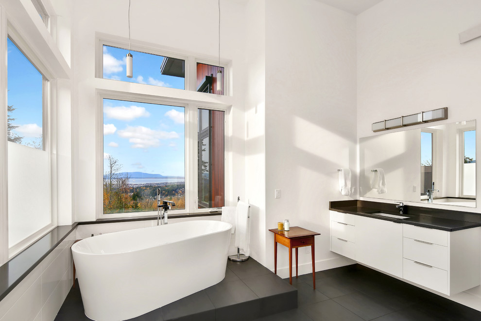 На фото: ванная комната в современном стиле с плоскими фасадами, белыми фасадами, белыми стенами, полом из сланца, врезной раковиной, столешницей из гранита, черным полом, черной столешницей, японской ванной и белой плиткой