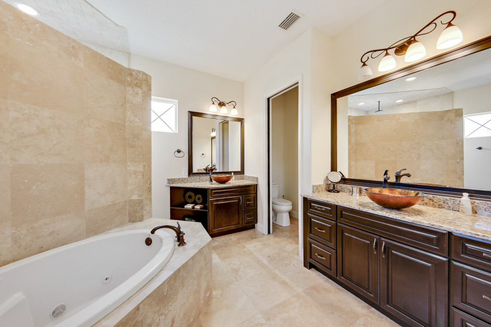 Design ideas for a coastal bathroom in Orlando with brown cabinets, a built-in bath, a walk-in shower, beige tiles, travertine tiles, beige walls, travertine flooring, a vessel sink, granite worktops, beige floors, an open shower, beige worktops, an enclosed toilet, double sinks and a built in vanity unit.