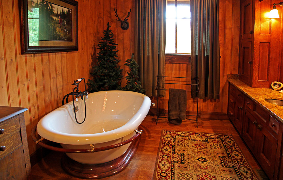 Exemple d'une salle de bain principale montagne en bois foncé de taille moyenne avec un lavabo encastré, un placard avec porte à panneau surélevé, un plan de toilette en granite, une baignoire indépendante, un mur marron et un sol en bois brun.