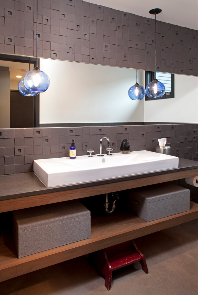 Bild på ett funkis badrum, med bänkskiva i täljsten, grå kakel, keramikplattor, betonggolv, ett fristående handfat, öppna hyllor och skåp i mellenmörkt trä