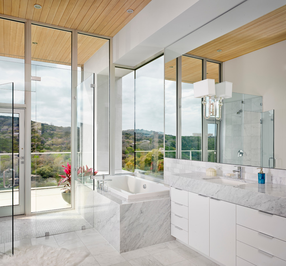 This is an example of a contemporary bathroom in Austin with a submerged sink, flat-panel cabinets, white cabinets, a corner bath, a corner shower, white tiles and white walls.