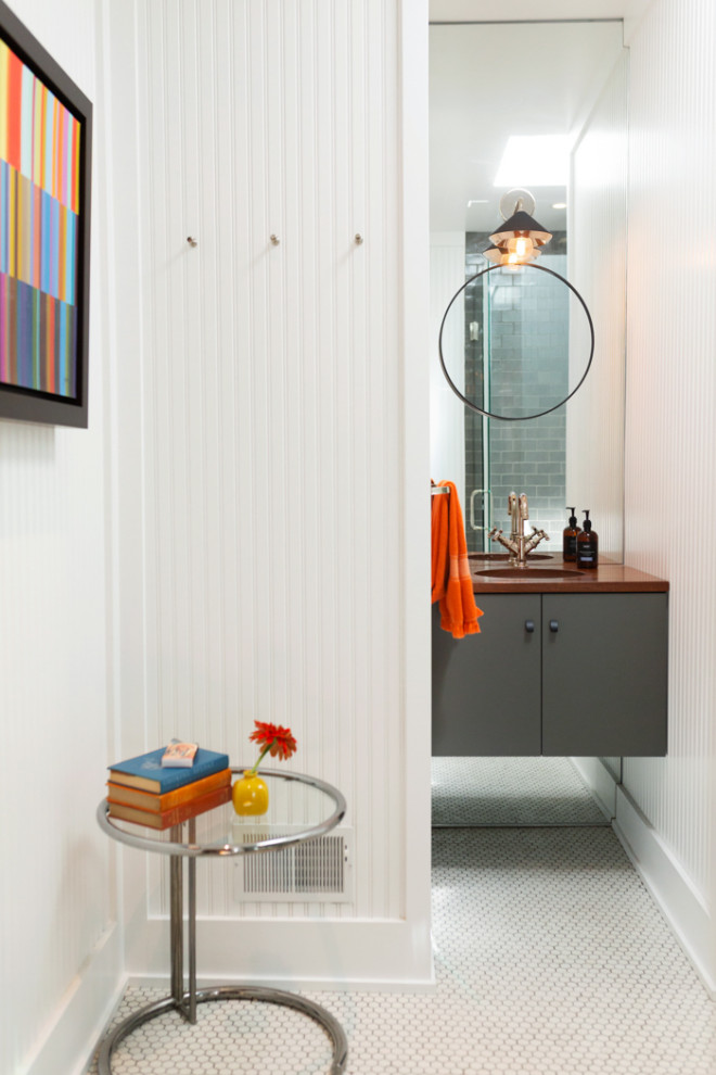 Cette image montre une salle de bain traditionnelle avec un placard à porte plane, des portes de placard grises, des carreaux de miroir, un mur blanc, un plan de toilette en bois, un sol blanc, un plan de toilette marron, meuble simple vasque, meuble-lavabo suspendu et du lambris.