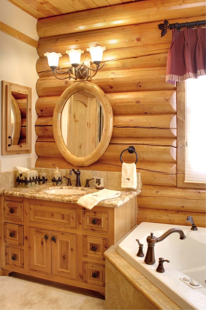 Foto di una stanza da bagno rustica di medie dimensioni con lavabo sottopiano, ante a filo, ante in legno chiaro, top in granito, vasca ad angolo, WC a due pezzi, piastrelle beige e piastrelle in pietra