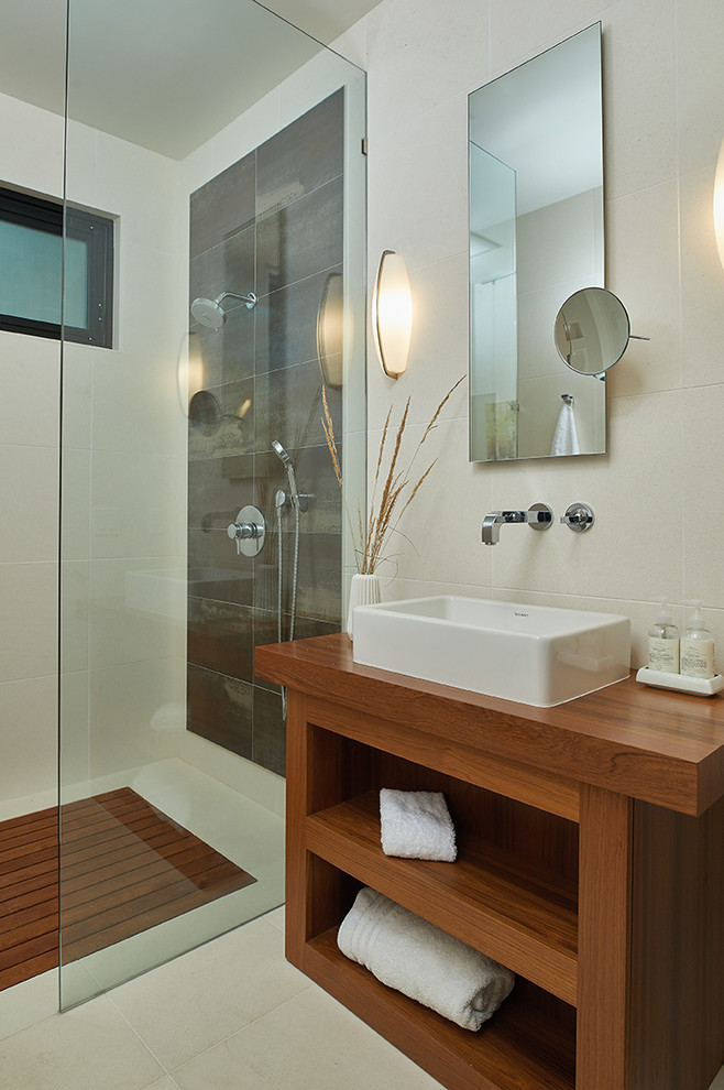 Bild på ett funkis brun brunt badrum med dusch, med öppna hyllor, skåp i mellenmörkt trä, grå kakel, beige kakel, träbänkskiva, med dusch som är öppen, en öppen dusch, beige väggar, ett fristående handfat och beiget golv
