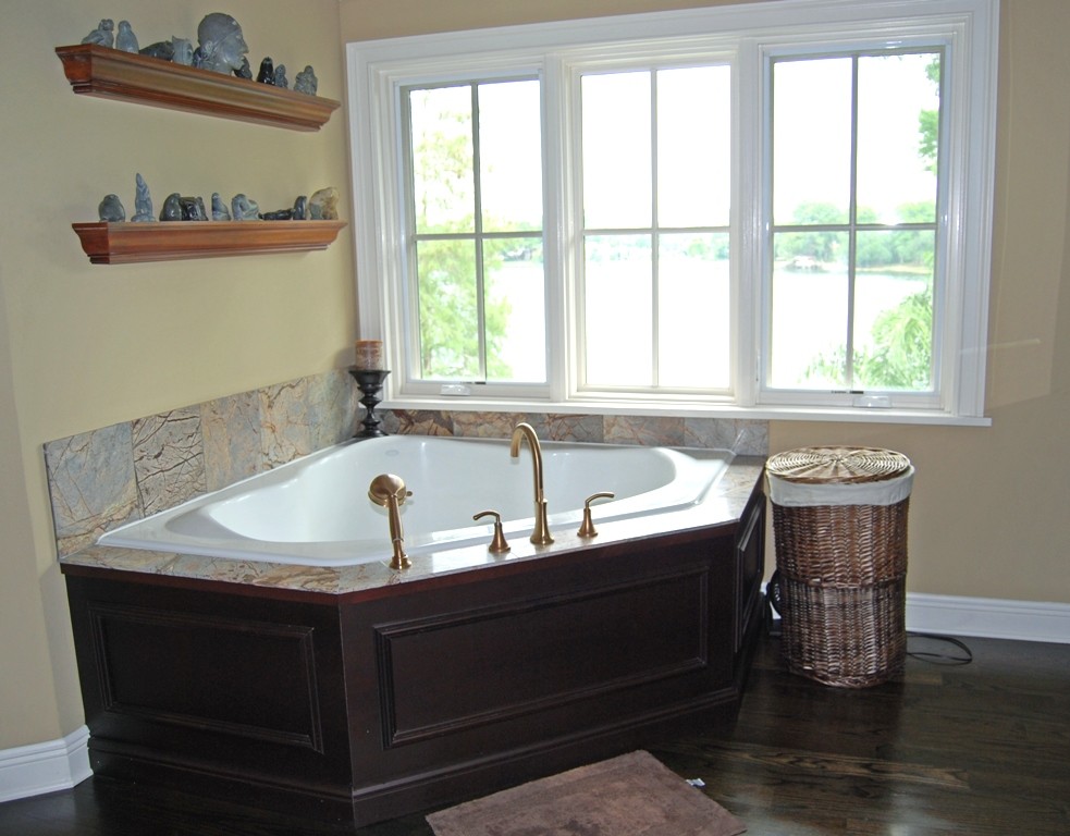 Cette image montre une grande salle de bain principale craftsman en bois foncé avec un placard avec porte à panneau surélevé, une baignoire d'angle, un mur beige, parquet foncé, un lavabo posé, un plan de toilette en granite et un sol marron.
