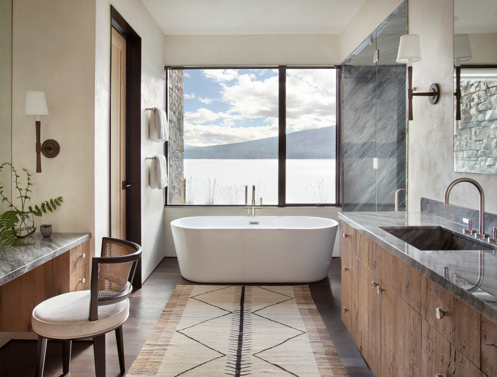 Bild på ett stort rustikt grå grått en-suite badrum, med släta luckor, skåp i mellenmörkt trä, ett fristående badkar, mörkt trägolv, ett integrerad handfat, granitbänkskiva, dusch med gångjärnsdörr, en dusch i en alkov, beige väggar och brunt golv