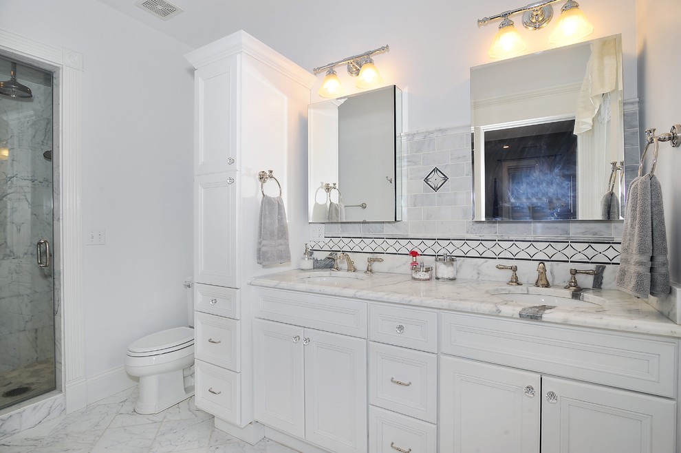 Photo of a large classic ensuite bathroom in Chicago with a submerged sink, recessed-panel cabinets, white cabinets, marble worktops, an alcove bath, a shower/bath combination, a two-piece toilet, white tiles, ceramic tiles, white walls and marble flooring.