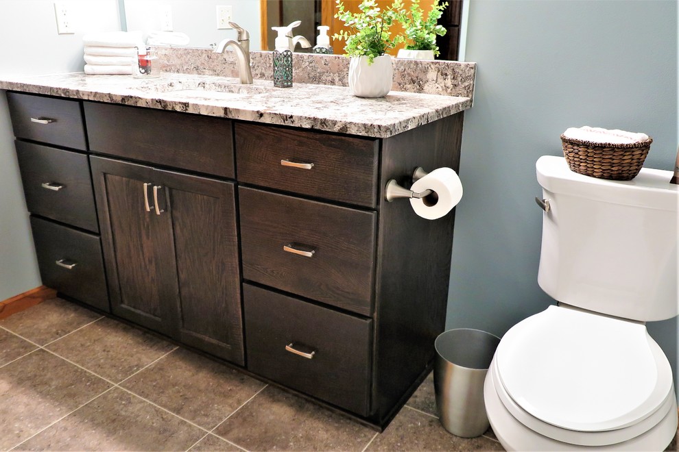 Photo of a medium sized classic ensuite bathroom in Minneapolis with recessed-panel cabinets, dark wood cabinets, an alcove bath, a two-piece toilet, white tiles, blue walls, vinyl flooring, a submerged sink, granite worktops, brown floors and grey worktops.