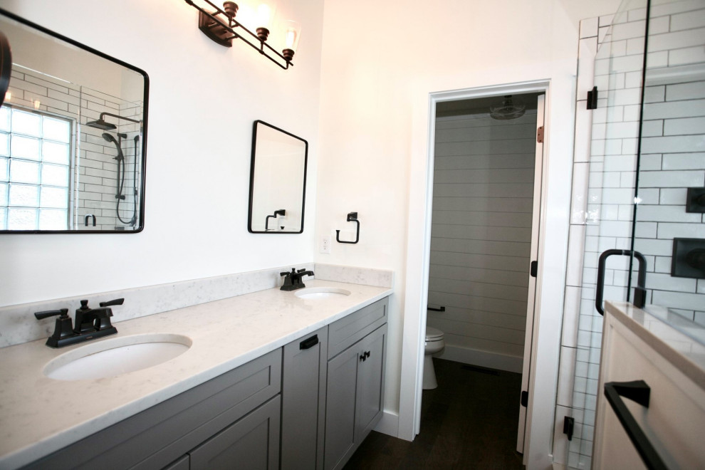 На фото: большая главная ванная комната в стиле кантри с фасадами в стиле шейкер, серыми фасадами, душем в нише, раздельным унитазом, белой плиткой, керамогранитной плиткой, белыми стенами, паркетным полом среднего тона, врезной раковиной, столешницей из искусственного кварца, коричневым полом, душем с распашными дверями, белой столешницей, сиденьем для душа, тумбой под две раковины, встроенной тумбой, потолком из вагонки и стенами из вагонки
