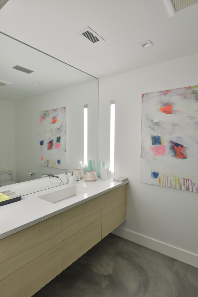 Ejemplo de cuarto de baño moderno de tamaño medio con armarios con paneles lisos, puertas de armario de madera clara, paredes blancas, suelo de cemento, aseo y ducha, lavabo integrado y encimera de acrílico