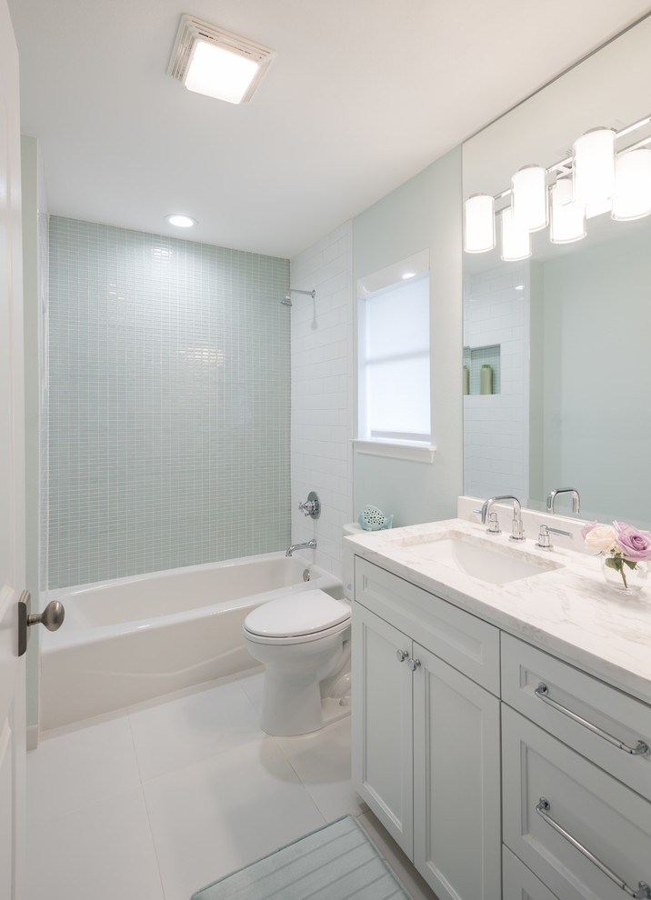 Idée de décoration pour une salle d'eau tradition de taille moyenne avec un placard à porte shaker, des portes de placard blanches, une baignoire en alcôve, un combiné douche/baignoire, WC à poser, un carrelage bleu, un carrelage en pâte de verre, un mur blanc, un sol en marbre, un lavabo encastré, un plan de toilette en marbre, un sol blanc et une cabine de douche avec un rideau.