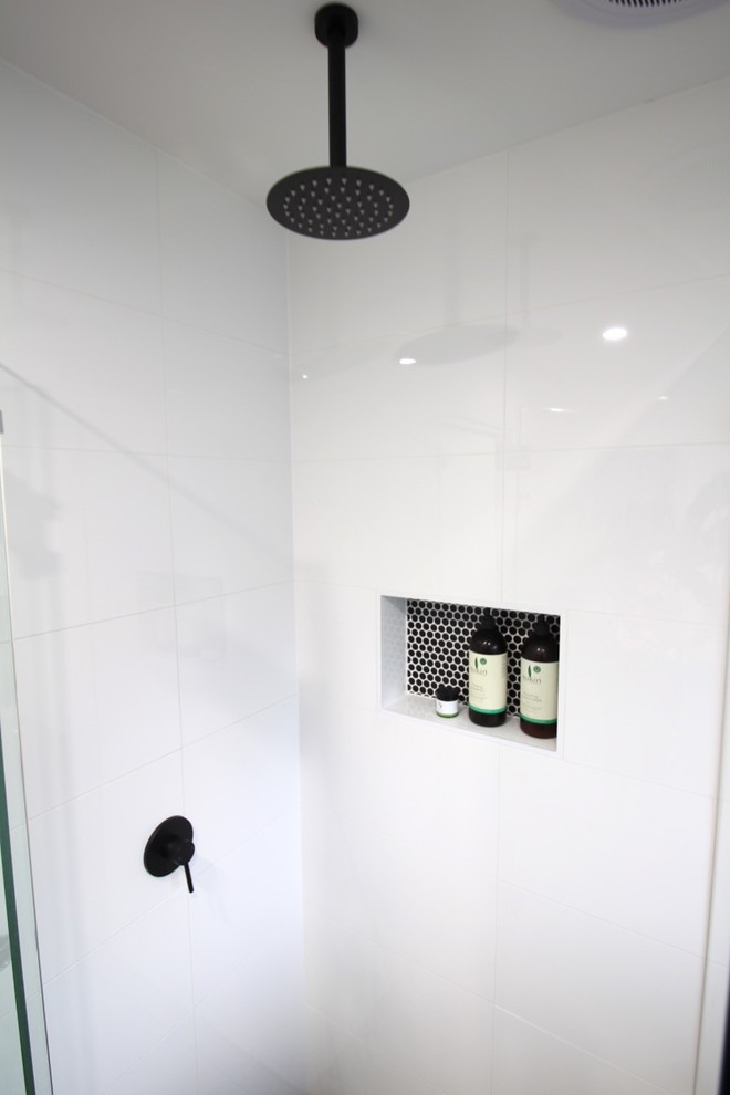This is an example of a contemporary ensuite bathroom in Brisbane with white cabinets, a corner shower, a wall mounted toilet, white tiles, cement tiles and white walls.