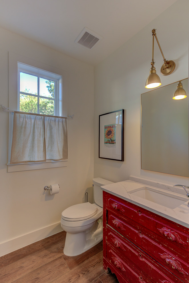 Foto på ett litet lantligt vit badrum med dusch, med möbel-liknande, röda skåp, en toalettstol med separat cisternkåpa, vita väggar, vinylgolv, ett undermonterad handfat, bänkskiva i kvartsit och brunt golv