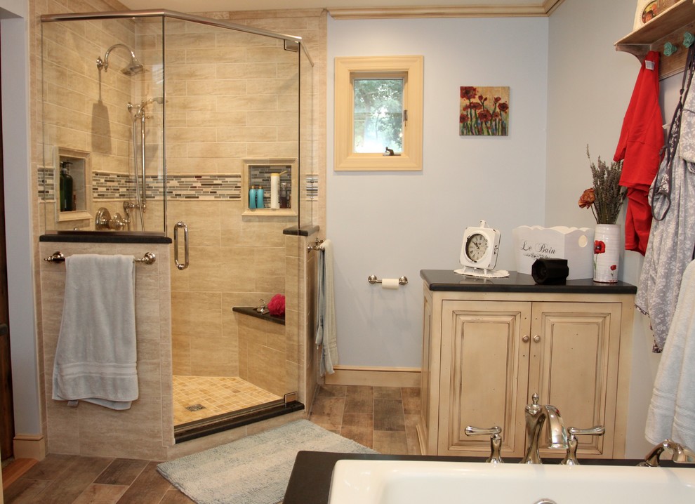 Exemple d'une salle de bain principale romantique en bois vieilli de taille moyenne avec un placard avec porte à panneau surélevé, une baignoire posée, une douche d'angle, WC séparés, un carrelage beige, des carreaux de porcelaine, un mur bleu, un sol en carrelage de porcelaine, un lavabo encastré, un plan de toilette en granite, un sol marron et une cabine de douche à porte battante.