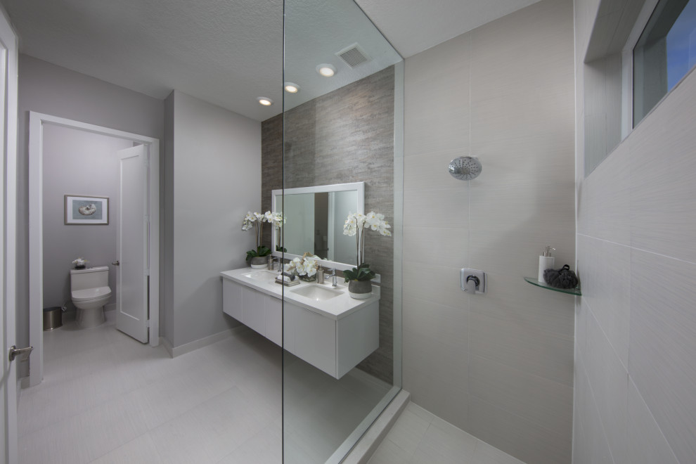 Exempel på ett stort modernt vit vitt en-suite badrum, med släta luckor, vita skåp, en öppen dusch, en toalettstol med hel cisternkåpa, grå kakel, porslinskakel, grå väggar, klinkergolv i porslin, ett integrerad handfat, bänkskiva i kvarts, grått golv och med dusch som är öppen
