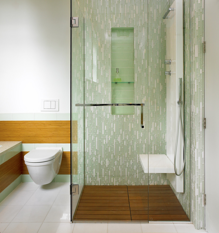 Modern inredning av ett badrum, med en kantlös dusch, en vägghängd toalettstol, grön kakel och glaskakel