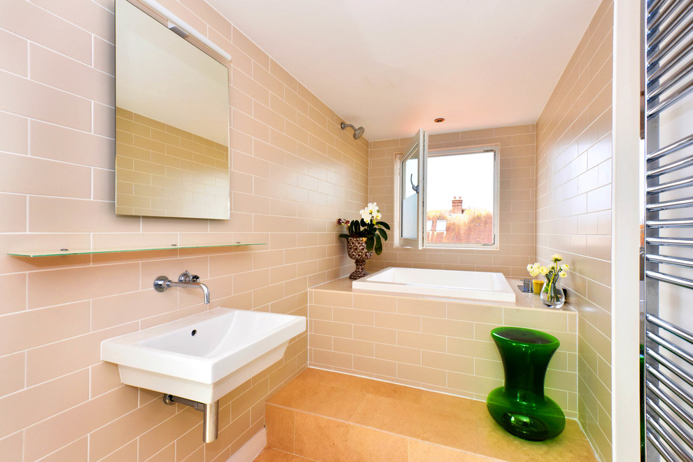 Photo of a small contemporary bathroom in Sussex with beige tiles, metro tiles, beige walls, a wall-mounted sink, a built-in bath, a shower/bath combination and beige floors.