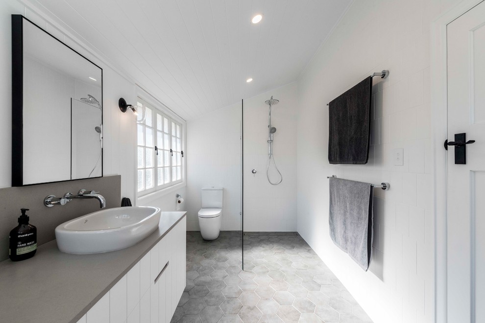 На фото: главная ванная комната в современном стиле с открытым душем, белой плиткой, открытым душем, серой столешницей, белыми фасадами, унитазом-моноблоком, керамической плиткой, белыми стенами, полом из цементной плитки, накладной раковиной и серым полом