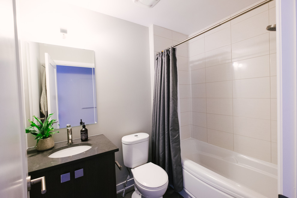 Photo of a medium sized contemporary shower room bathroom in Ottawa with flat-panel cabinets, black cabinets, an alcove bath, a shower/bath combination, a two-piece toilet, white tiles, porcelain tiles, grey walls, porcelain flooring, a submerged sink, solid surface worktops, multi-coloured floors and a shower curtain.