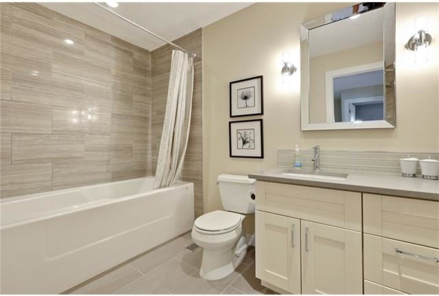 Inredning av ett modernt mellanstort en-suite badrum, med luckor med upphöjd panel, vita skåp, ett fristående badkar, en toalettstol med separat cisternkåpa, grå kakel, glasskiva, beige väggar, klinkergolv i keramik, ett undermonterad handfat och bänkskiva i kvartsit