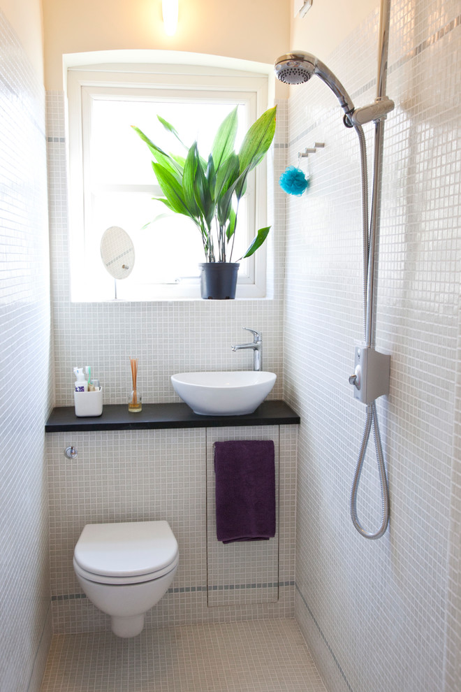 Foto på ett litet funkis badrum med dusch, med våtrum, en vägghängd toalettstol, vit kakel, mosaik, vita väggar, mosaikgolv, ett konsol handfat och vitt golv