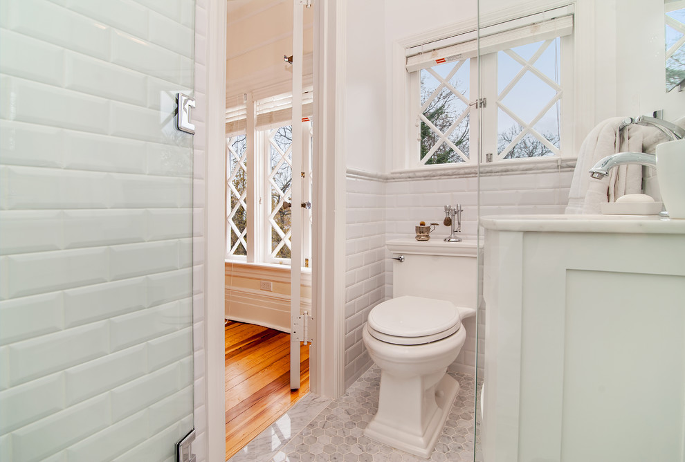 На фото: ванная комната в классическом стиле с фасадами островного типа, белыми фасадами, отдельно стоящей ванной, угловым душем, унитазом-моноблоком, серой плиткой, плиткой мозаикой, белыми стенами, мраморным полом, врезной раковиной и мраморной столешницей