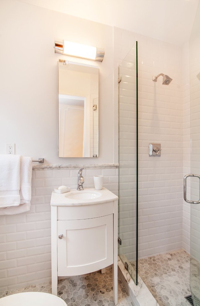 Photo of a classic bathroom in New York with freestanding cabinets, white cabinets, a freestanding bath, a corner shower, a one-piece toilet, grey tiles, mosaic tiles, white walls, marble flooring, a submerged sink and marble worktops.
