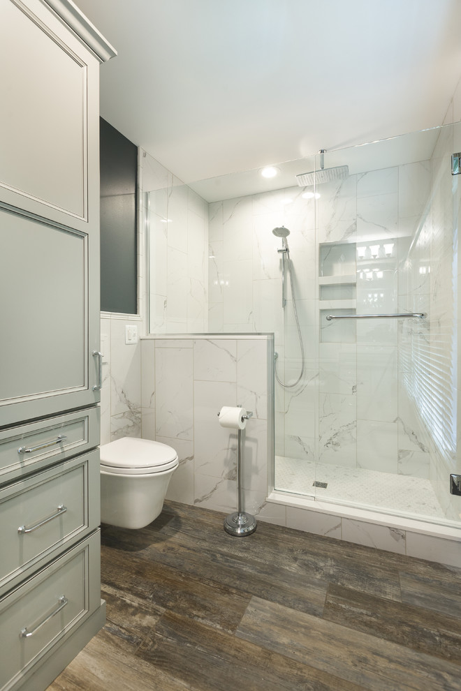 Design ideas for a large traditional shower room bathroom in Detroit with recessed-panel cabinets, grey cabinets, an alcove shower, a wall mounted toilet, white tiles, marble tiles, white walls, dark hardwood flooring, brown floors and a hinged door.