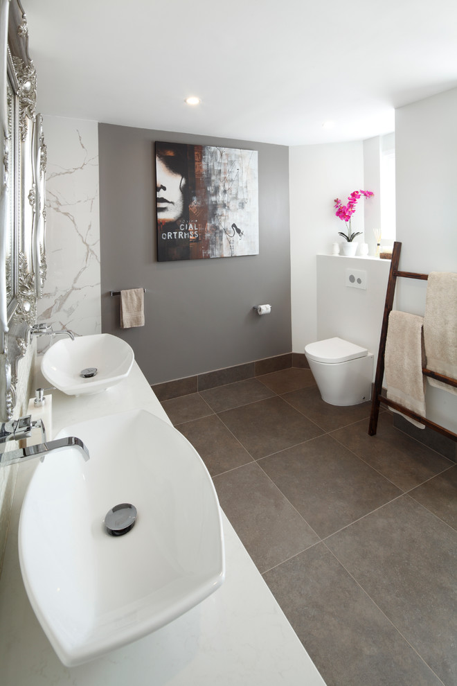 Cette image montre une grande salle de bain principale minimaliste avec un placard à porte plane, des portes de placard grises, WC à poser, une vasque, un plan de toilette en surface solide et un sol gris.