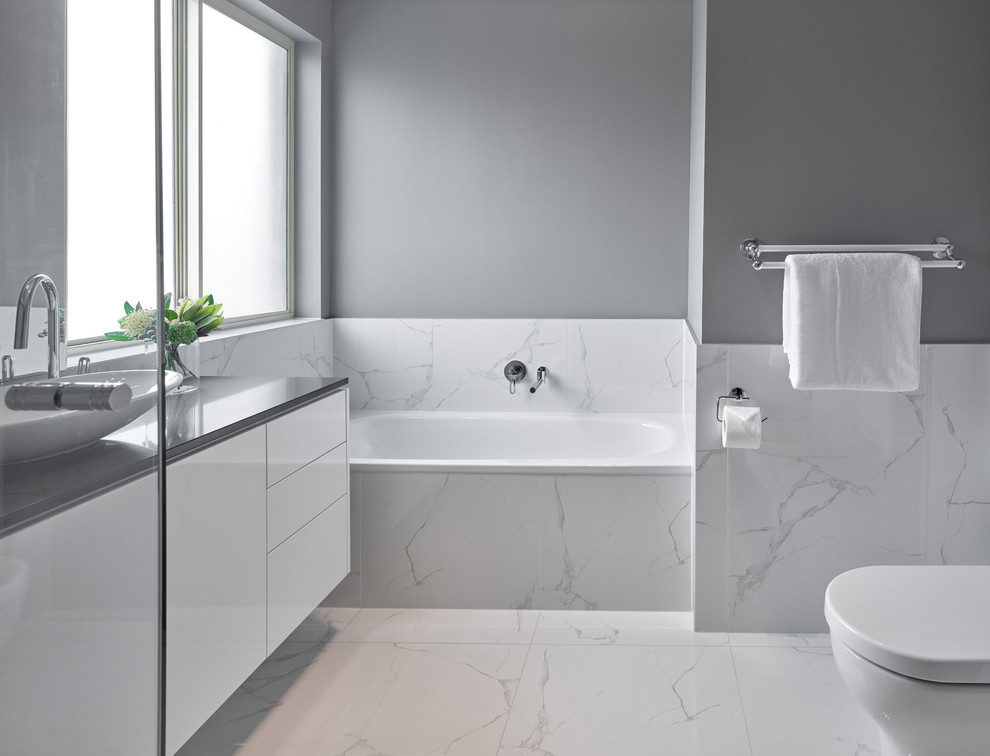 This is an example of a large classic ensuite bathroom in Other with flat-panel cabinets, white cabinets, a built-in bath, a walk-in shower, a two-piece toilet, white tiles, porcelain tiles, grey walls, porcelain flooring, a vessel sink, engineered stone worktops, white floors, an open shower and grey worktops.