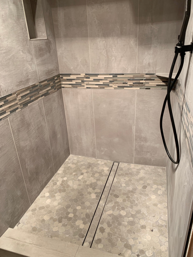 Klassisk inredning av ett badrum, med grå kakel, porslinskakel, grå väggar, klinkergolv i småsten och flerfärgat golv