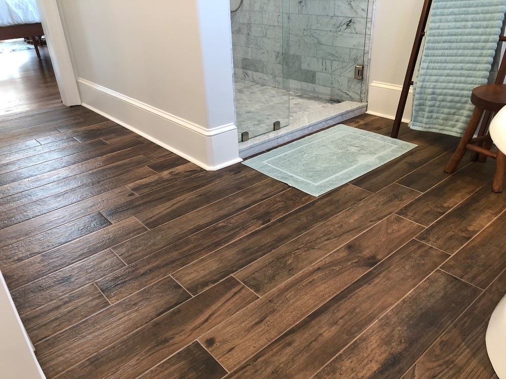 Bathroom - large contemporary master gray tile and stone tile medium tone wood floor and brown floor bathroom idea in Philadelphia with flat-panel cabinets, white cabinets, a one-piece toilet, gray walls, a console sink, granite countertops, a hinged shower door and gray countertops