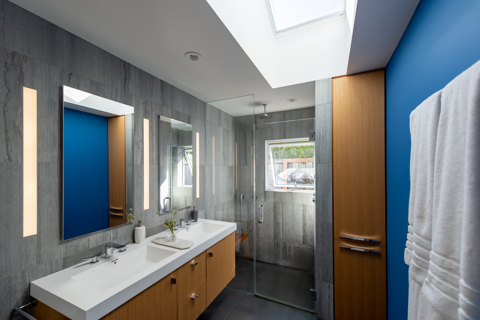Exempel på ett modernt vit vitt badrum med dusch, med släta luckor, skåp i ljust trä, en dusch i en alkov, grå kakel, blå väggar, ett integrerad handfat, grått golv och dusch med gångjärnsdörr