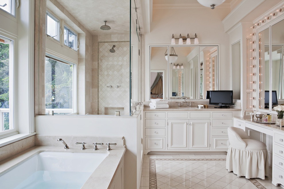 ロサンゼルスにあるトラディショナルスタイルのおしゃれな浴室 (落し込みパネル扉のキャビネット、白いキャビネット、アンダーマウント型浴槽、アルコーブ型シャワー、ベージュのタイル、白い床、照明) の写真
