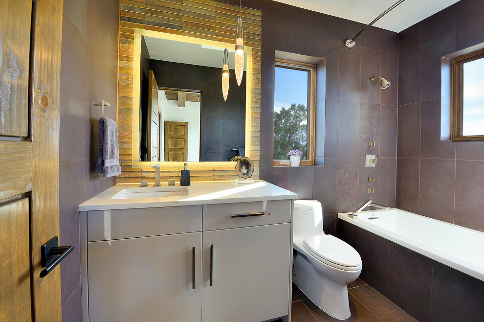 Example of a mid-sized southwest master brown tile and cement tile brown floor alcove bathtub design in Albuquerque with flat-panel cabinets, gray cabinets, a one-piece toilet, an undermount sink, quartz countertops and white countertops
