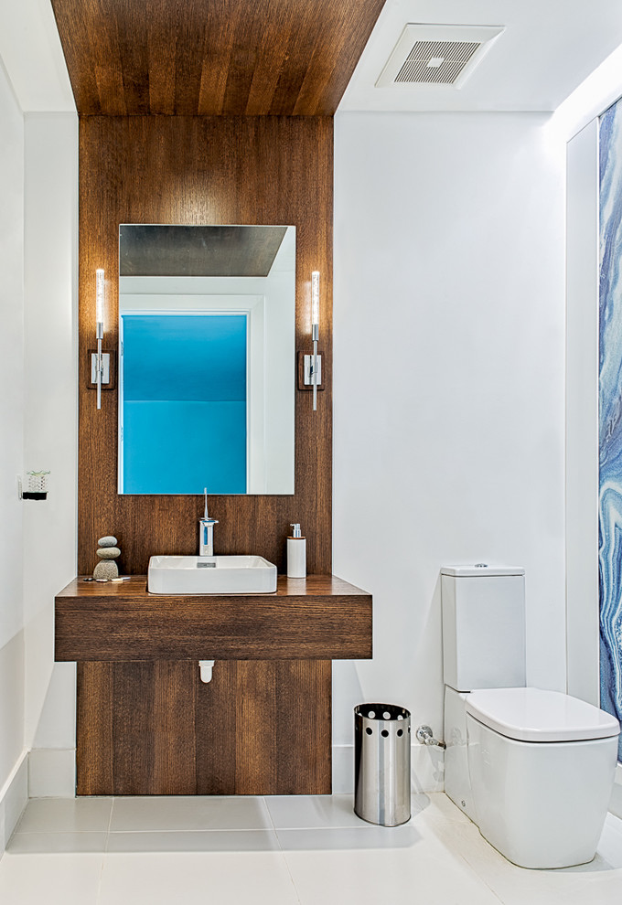 Cette image montre une salle d'eau design en bois brun de taille moyenne avec un placard sans porte, WC séparés, un mur bleu, un sol en carrelage de porcelaine, une vasque et un plan de toilette en bois.