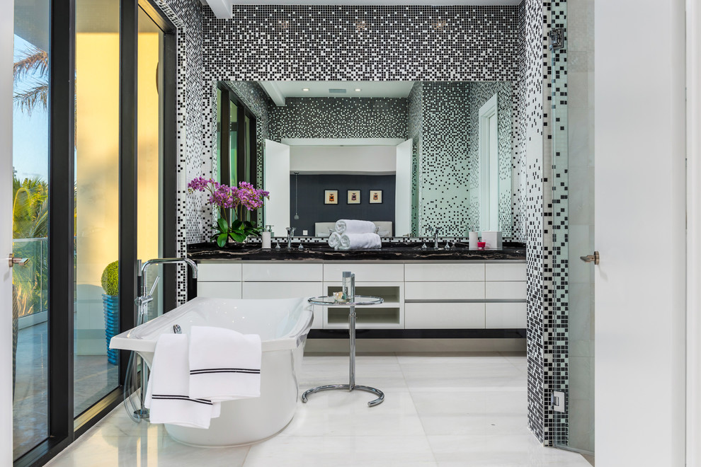 Idée de décoration pour une salle de bain principale design avec un placard à porte plane, des portes de placard blanches, une baignoire indépendante, un carrelage noir, un carrelage noir et blanc, un carrelage multicolore, un carrelage blanc, mosaïque, un sol blanc et un plan de toilette noir.