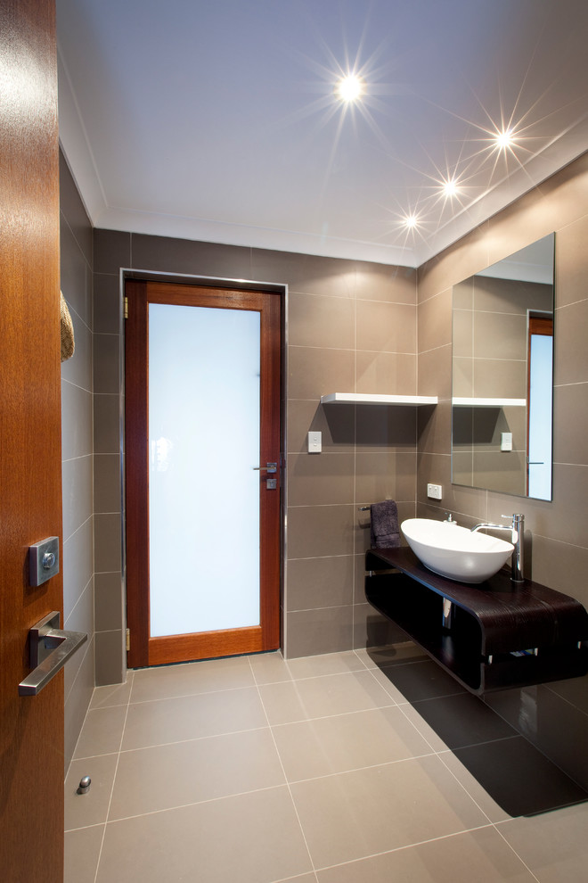 Стильный дизайн: ванная комната среднего размера в современном стиле с настольной раковиной, фасадами цвета дерева среднего тона, столешницей из искусственного кварца, отдельно стоящей ванной и серой плиткой - последний тренд